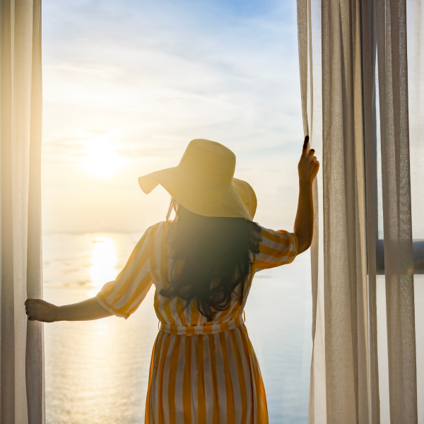 Mujer en vestido amarillo y sombrero mirando por la ventana hacia el oc茅ano